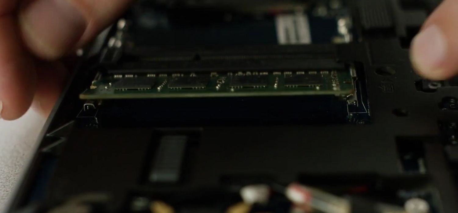 Uma pessoa remove os clipes laterais de um módulo RAM Crucial para removê-lo de um laptop